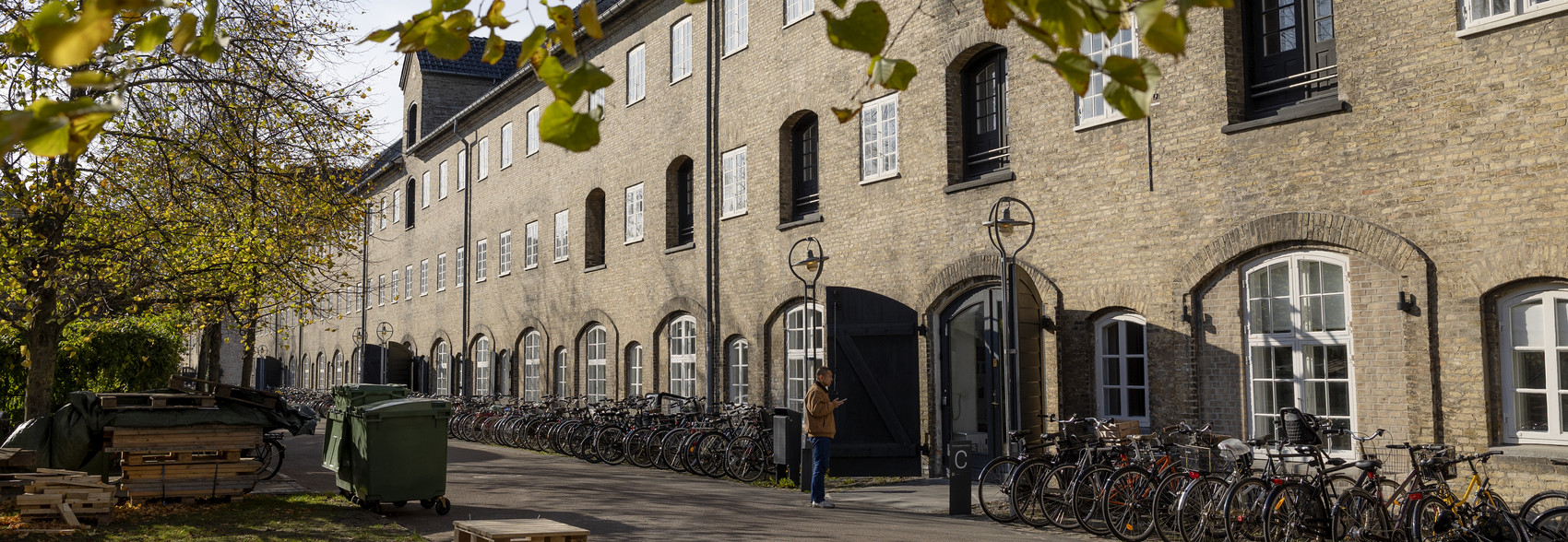 ng brick building with bicycles along the façade, framed by autumn trees.