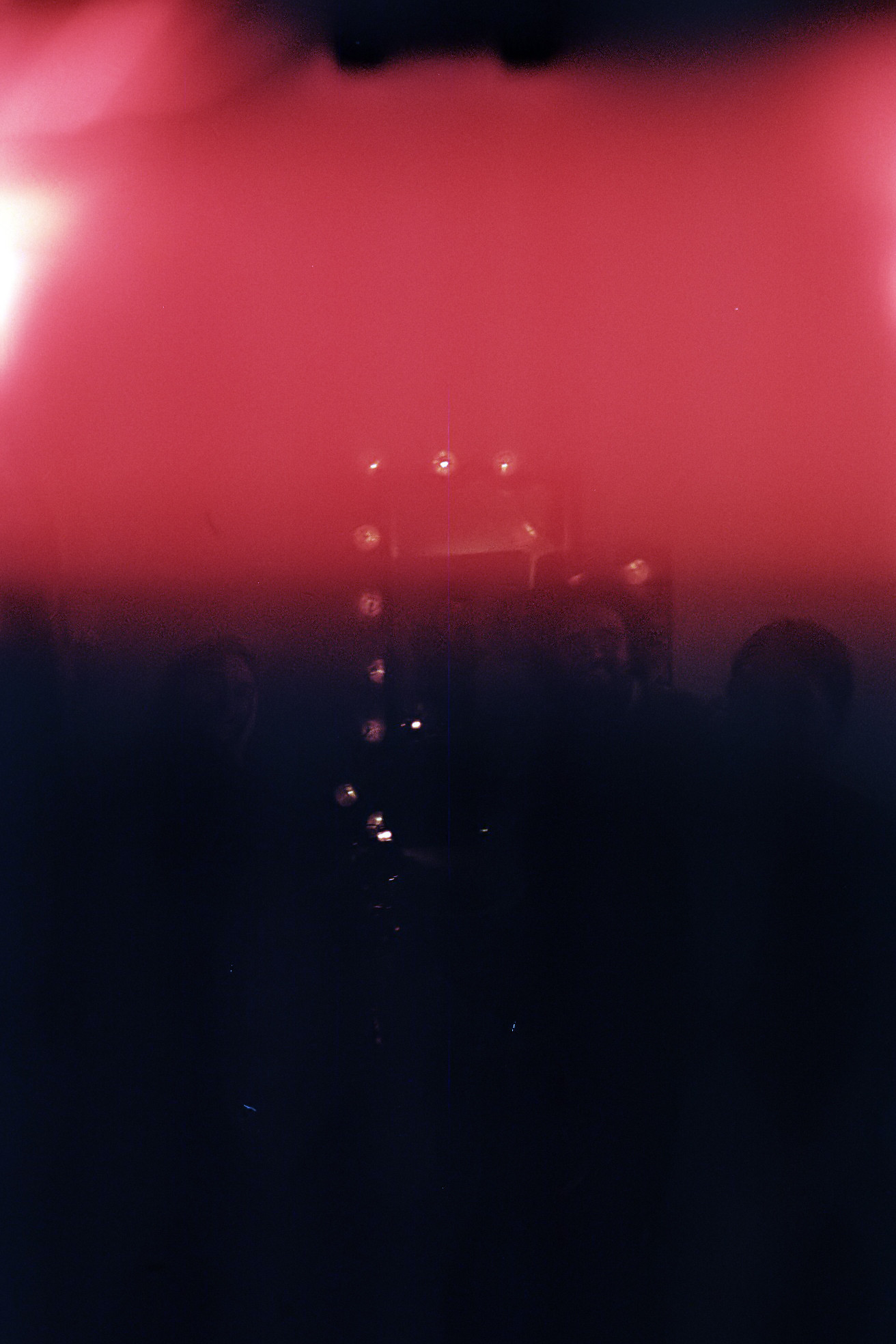 Photograph of a group of people sitting around a table. The image is obstructed by a black and red patch. Only what appears to be a string of lights and the shilouettes of three heads in the center are visible.  