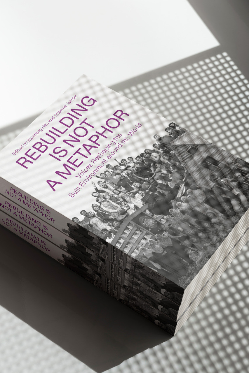 Stack of books titled ‘Rebuilding Is Not a Metaphor’ lying in patterned light and shadow.