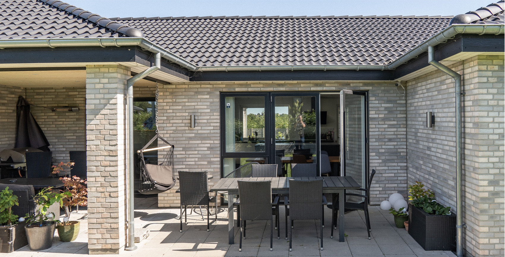 Moderne murstenshus med overdækket terrasse og havemøbler.