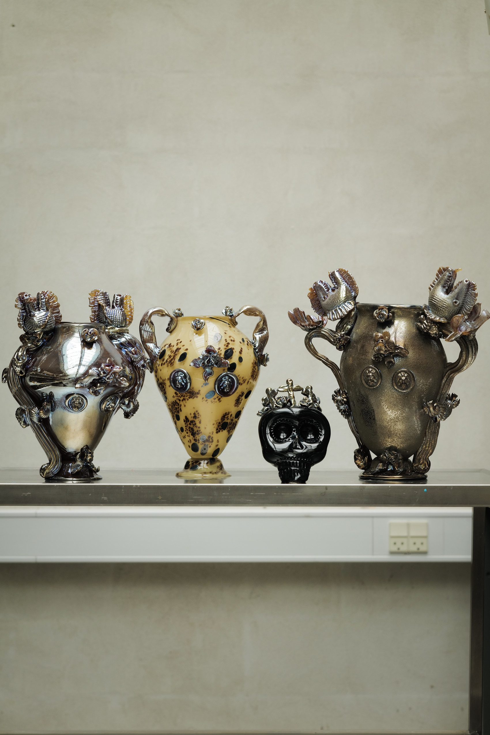 Beautiful art pieces on display on a metallic rolling kitchen table. The bourgeois beauty of the vessels clashes immaculately with the industrial roughness of one of the working classes tools