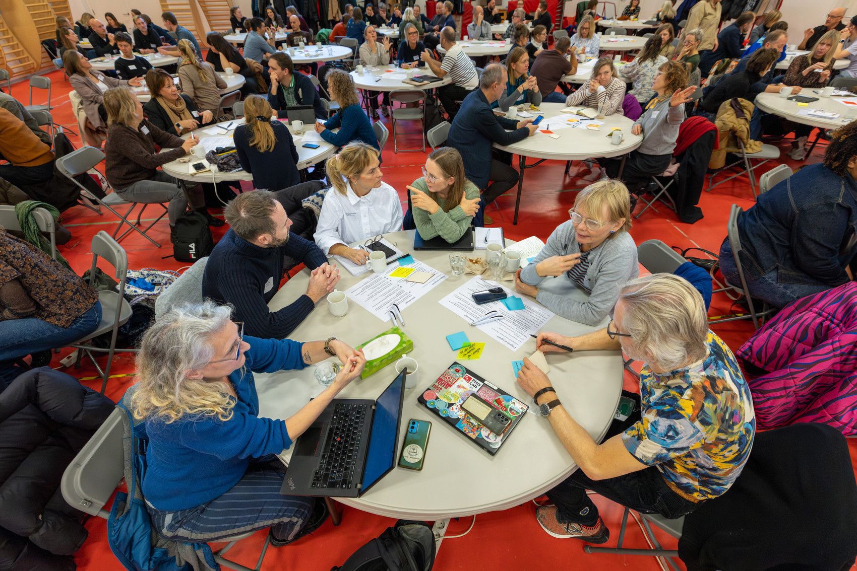 Mange deltagere sidder ved runde borde og diskuterer i en workshop.